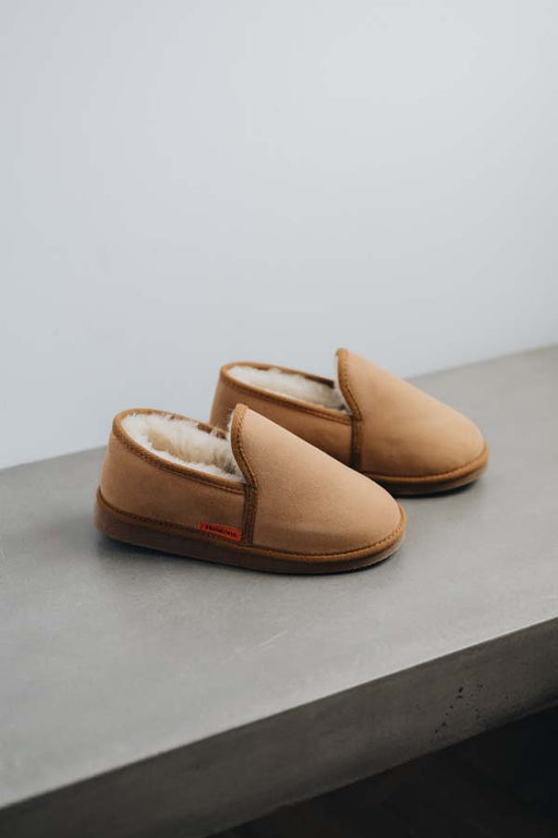 Pair of tan sheepskin slippers with shearling lining on a concrete surface.