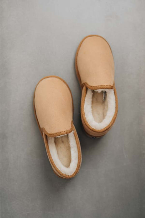 Birds eye view of a pair of tan sheepskin slippers with white wool lining on a stone bench
