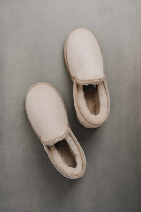 Birds eye view of a pair of vanilla sheepskin slippers on a grey stone background