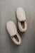 Birds eye view of a pair of vanilla sheepskin slippers on a grey stone background