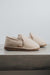 Profile view of a pair of vanilla sheepskin slippers on a concrete surface 
