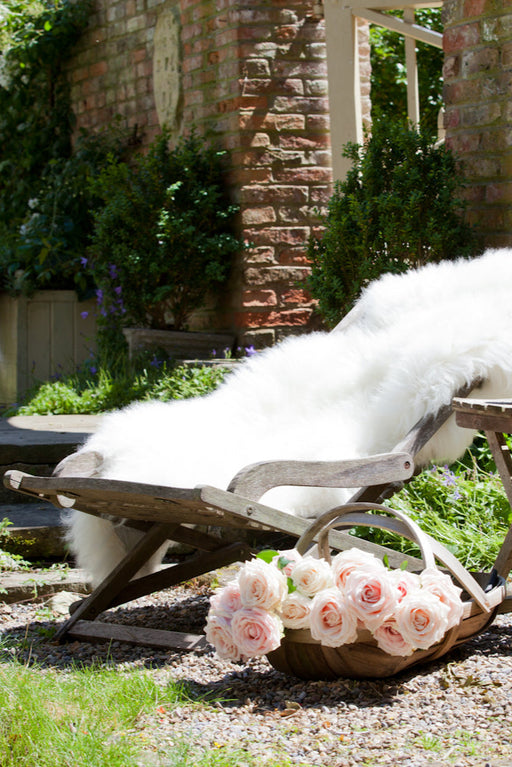 A Dense and plush Natural White British Sheepskin Rug softening up a deckchair in an English Country Garden on a beautiful summers day.