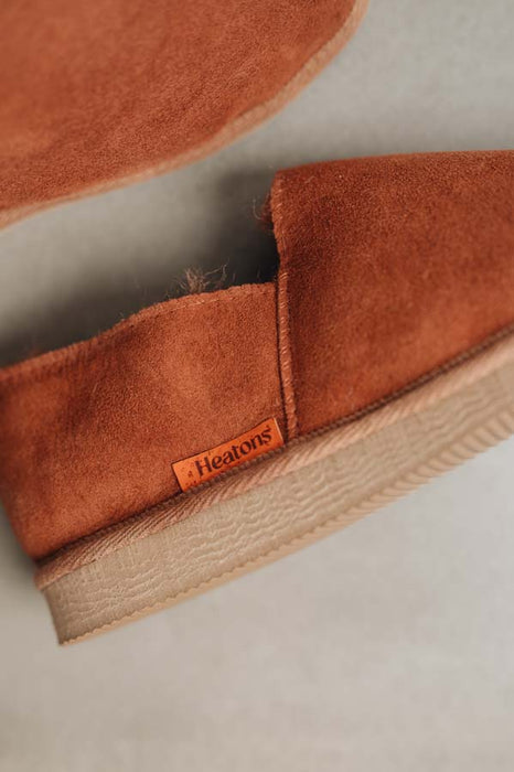 Close up of rust coloured loafer style sheepskin slipper with orange cork label showing the Heatons brand