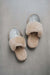 A pair of open-toe slippers with fluffy beige Merino sheepskin trim and metallic silver uppers, photographed from above on a neutral stone surface.