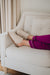 Women in purple pyjamas wearing Veronica Vanilla Sheepskin Slippers withthe collar folded up on a vanilla coloured sofa