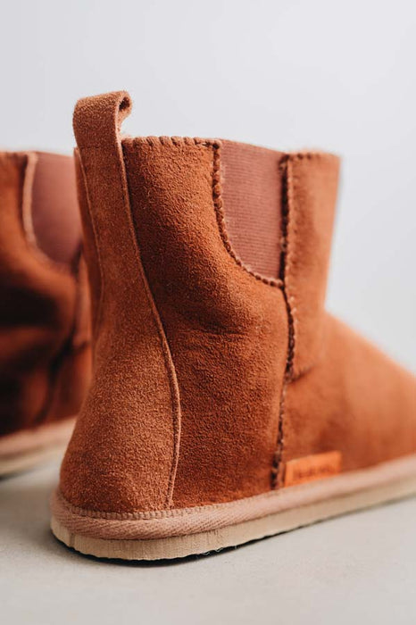 Close-up of rust coloured sheepskin boots on a light concrete background.