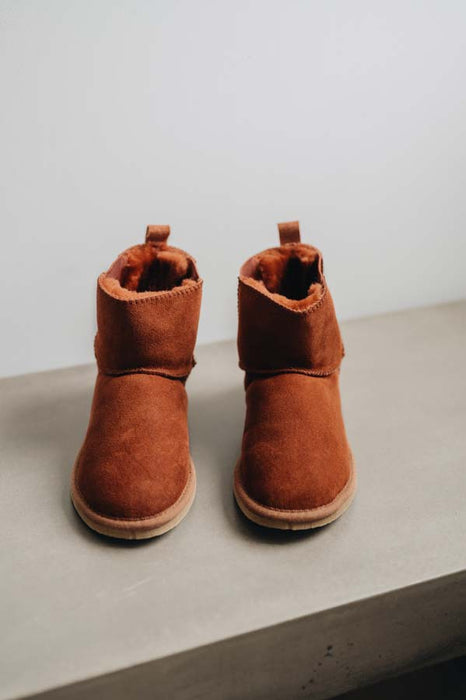 Pair of rust coloured sheepskin slipper boots on a light grey surface with a white background