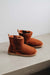 Pair of rust coloured sheepskin slipper boots on a light grey surface with a white background