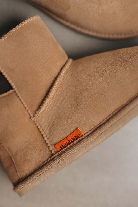 Close-up of tan sheepskin boots with a visible orange cork Heatons brand logo on a neutral background
