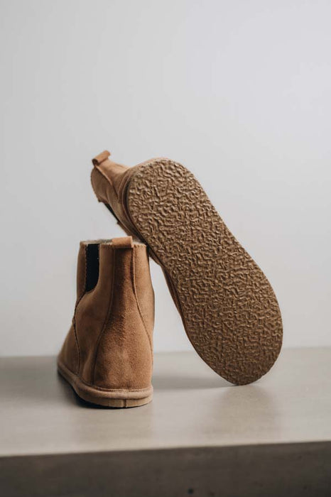 Tan sheepskin boot with textured rubber sole on a light grey background