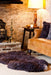 Cosy Brown British Sheepskin Rug, in front of the fire on the floor with accent Sheepskin cushions on a  leather sofa next to it. 